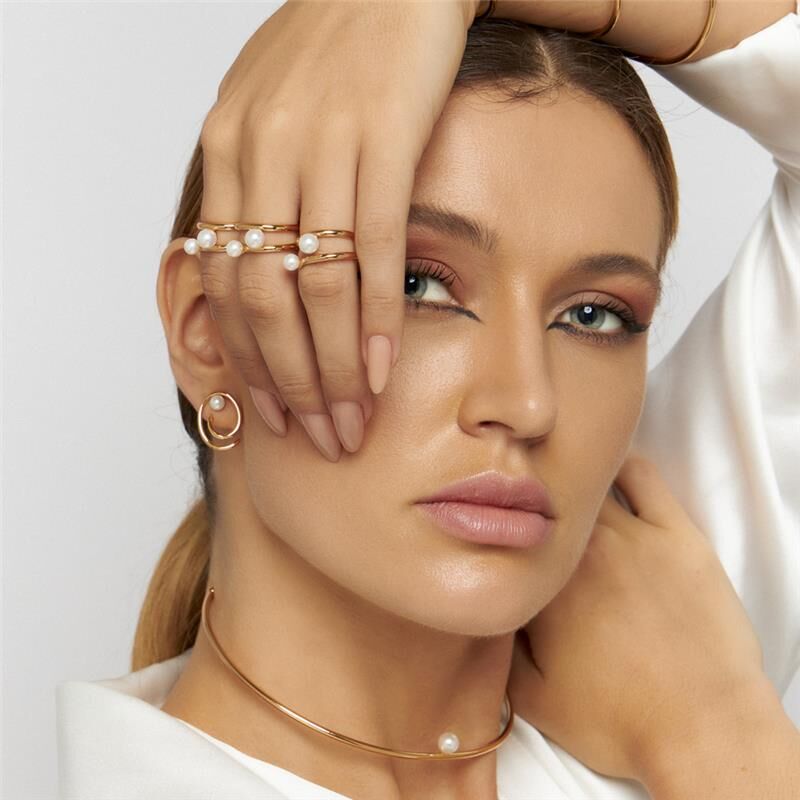 Woman wearing two gold rings with white pearls hand gently resting on face