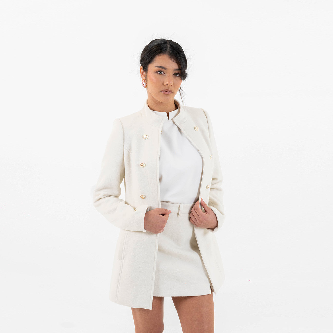 Model wearing Galli The Label Ivory Chic Set with off-white blazer and mini skirt featuring sleek gold buttons and a collarless cut.