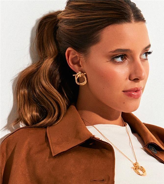 Model wearing Gilded Knot Stud Earrings with brown jacket
