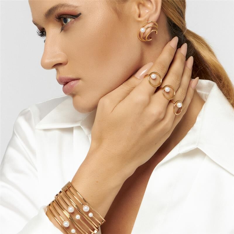 Woman wearing hollow gold pearl ring with stacked bangles and white blouse
