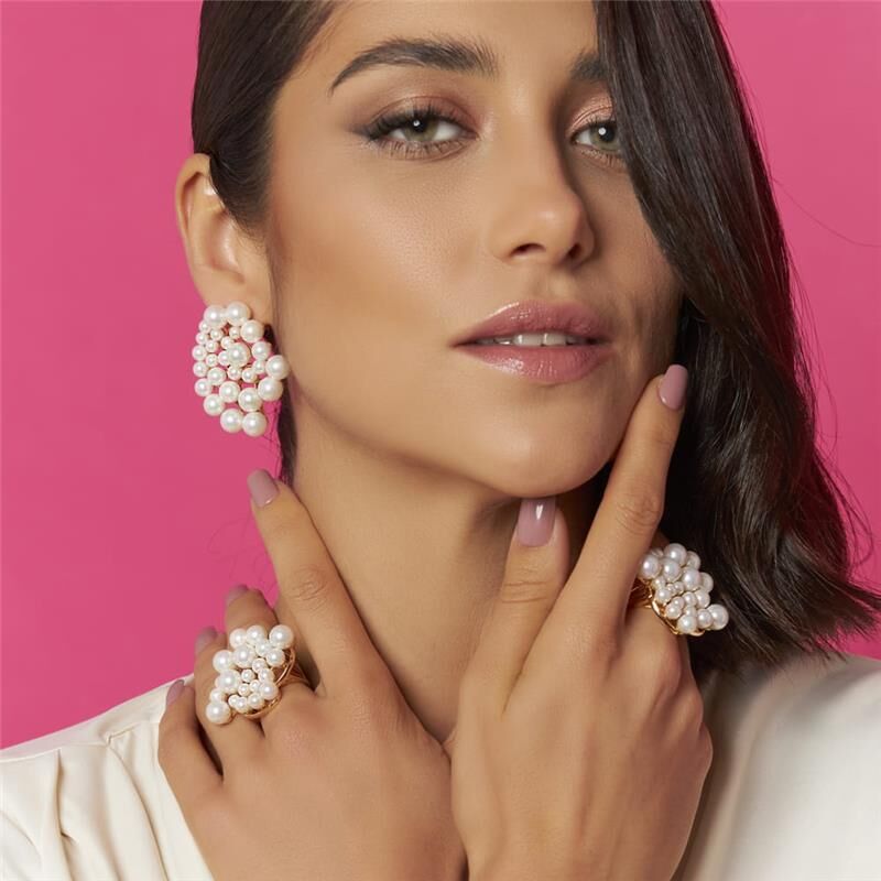 Model wearing spiral pearl earrings and statement rings against a pink background
